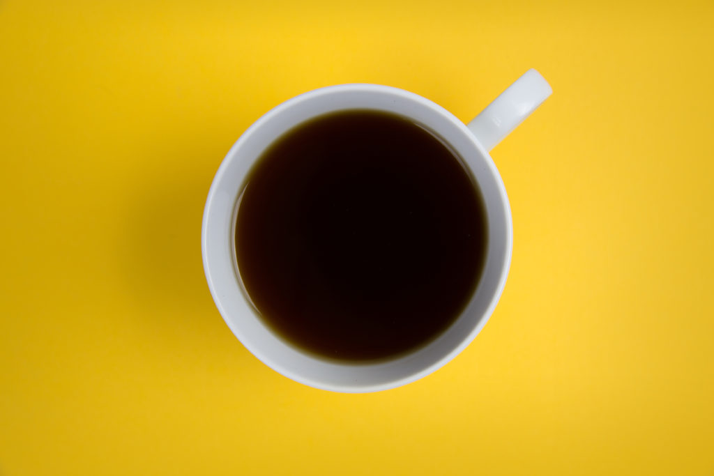 Overhead view of a cup of black coffee in a white mug on a yellow table