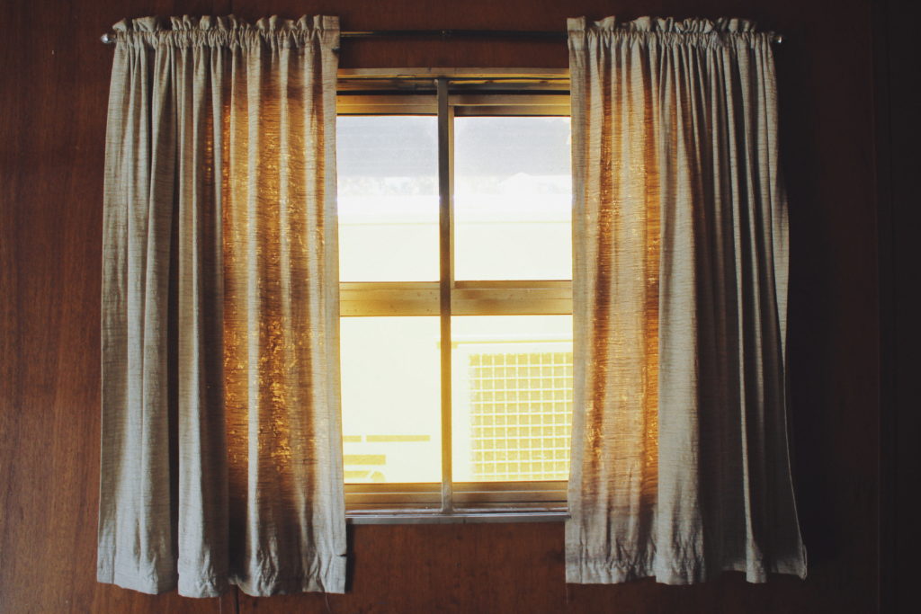 Window with partially open grey drapes on a sunny day