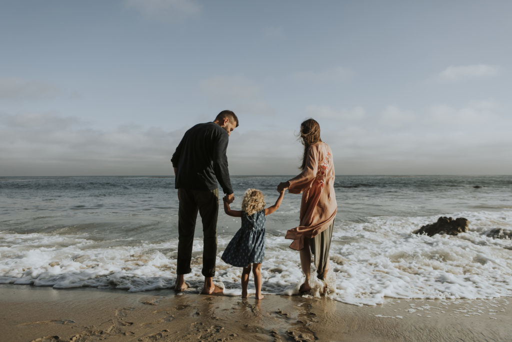 Young mother and father with a daughter on the shore with their bare feet in the water.