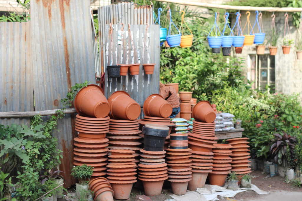 Stacks of flower pots in front of corrugated steel fence and hedges.