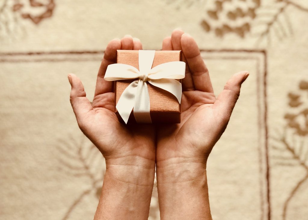 A pair of hands laid out holding a small gift with bronze wrapping paper and cream bow.