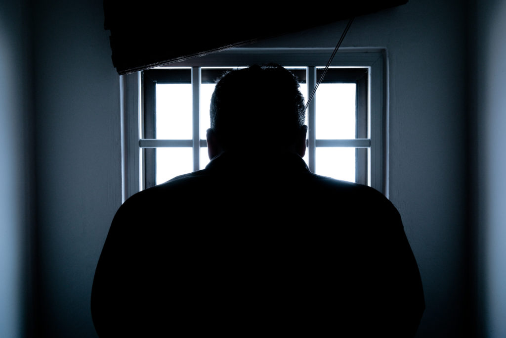 Silhouette of a man opening blinds looking through a window on a door.