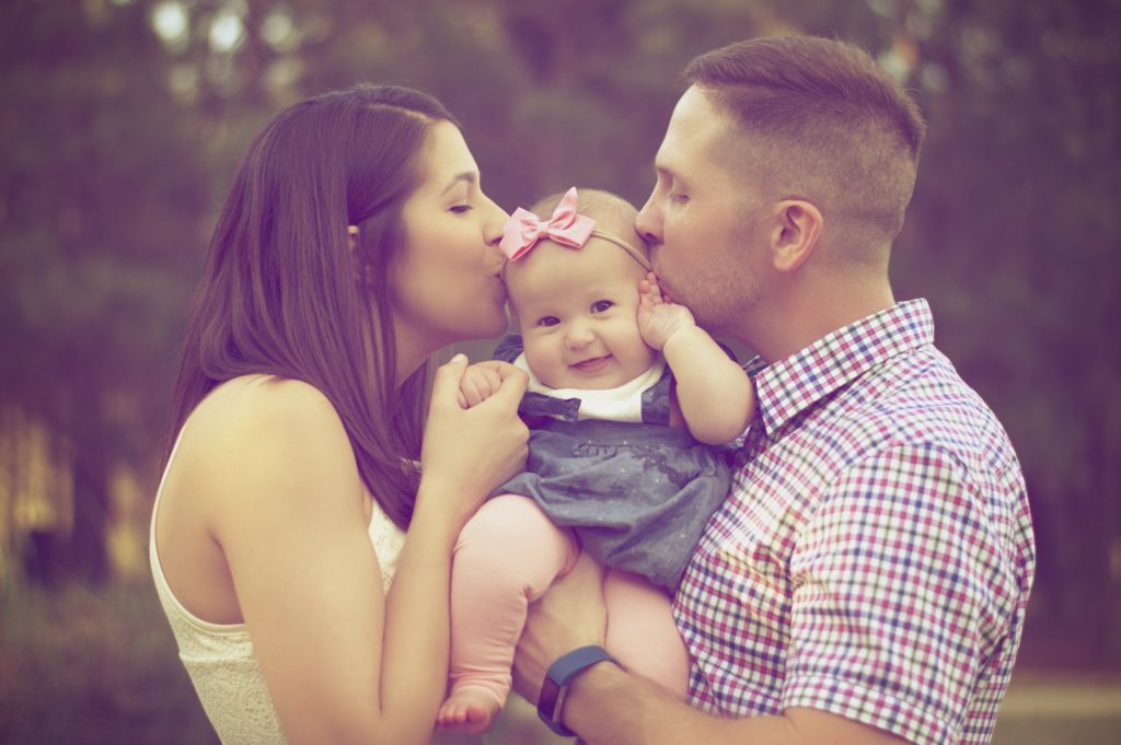 Young mother and father holding their daughter between them whilst kissing her.