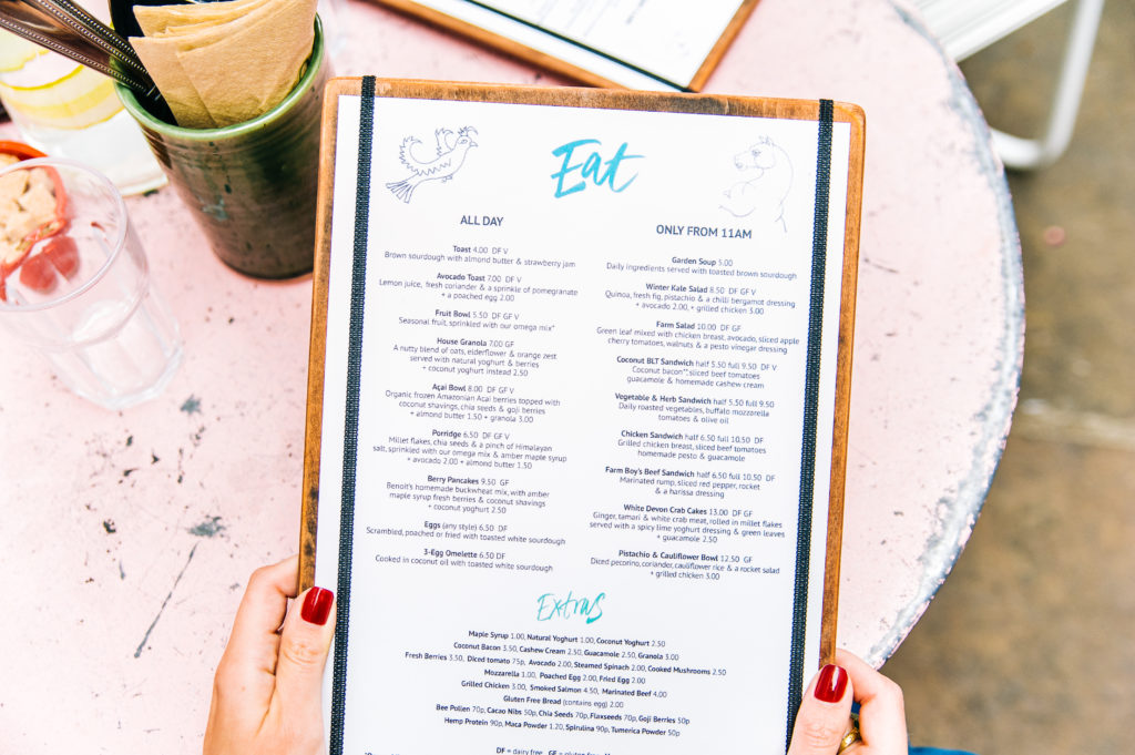 A woman's hand holding a restaurant menu in an outdoor patio cafe above a pink table.