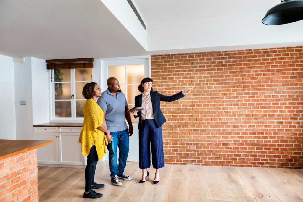 A realtor showing a house with interior brick walls to a prospective house-buying couple.