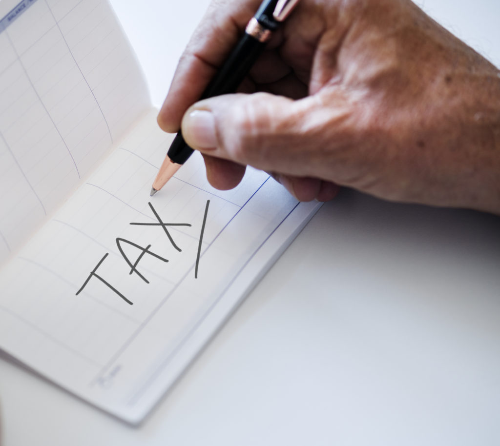 A man holding a pen above the word "tax" in a balance book.