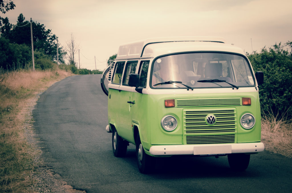 A lime green Volkswagen bus driving around a curve on a country road.
