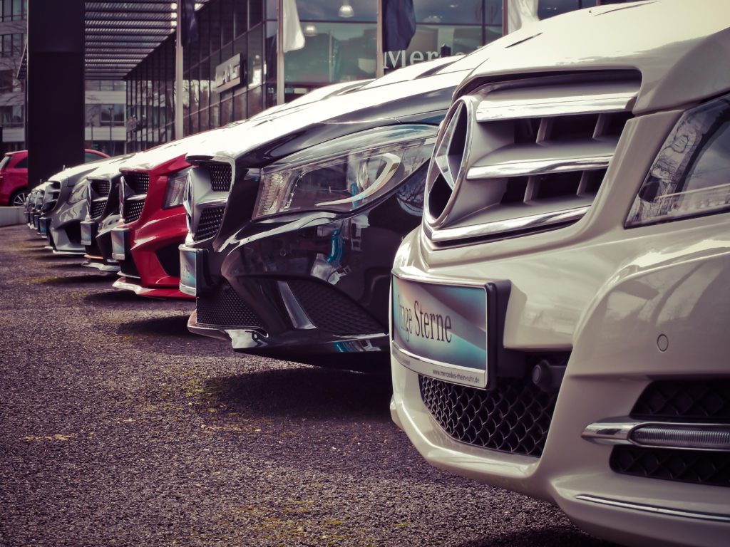 A line of Mercedes cars' front ends in a car dealership parking lot.