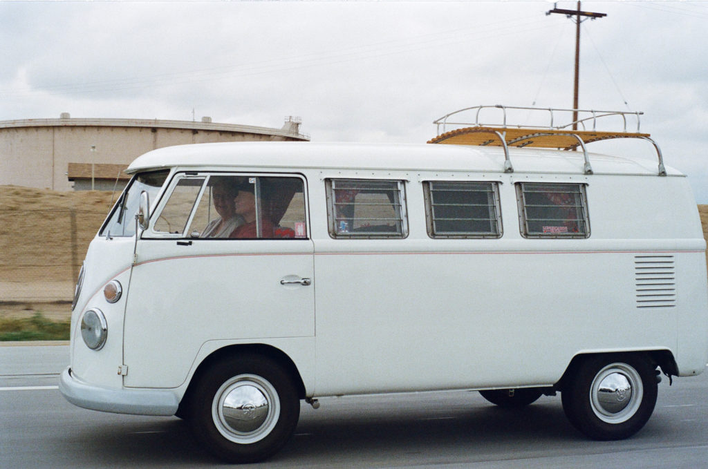 A white classic Volkswagen bus driving on an overcast day.