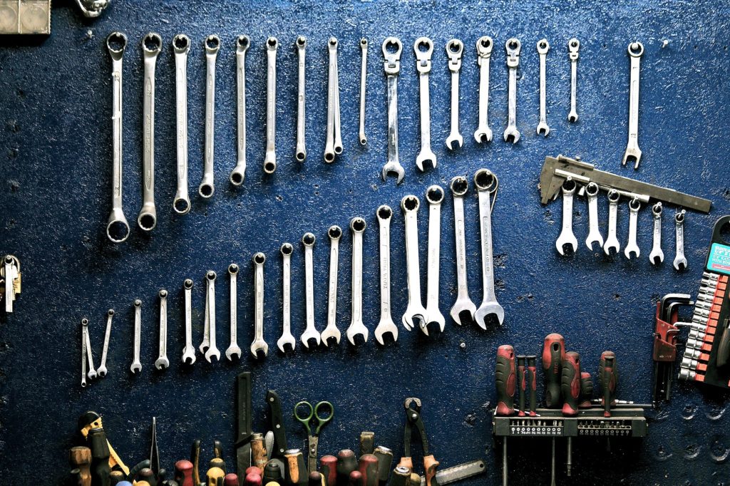 Mechanic wrenches hanging on a blue wall with other tools in wall-mounted holders.