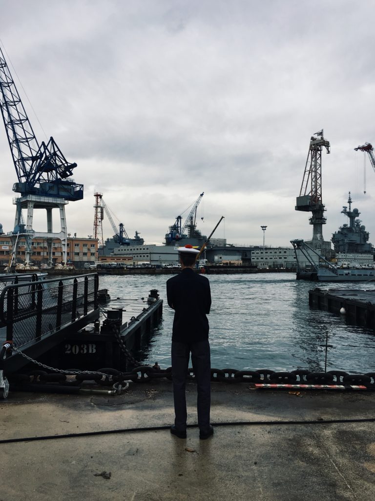 A sailor standing on docks looking out at a bay full of cranes and ships.