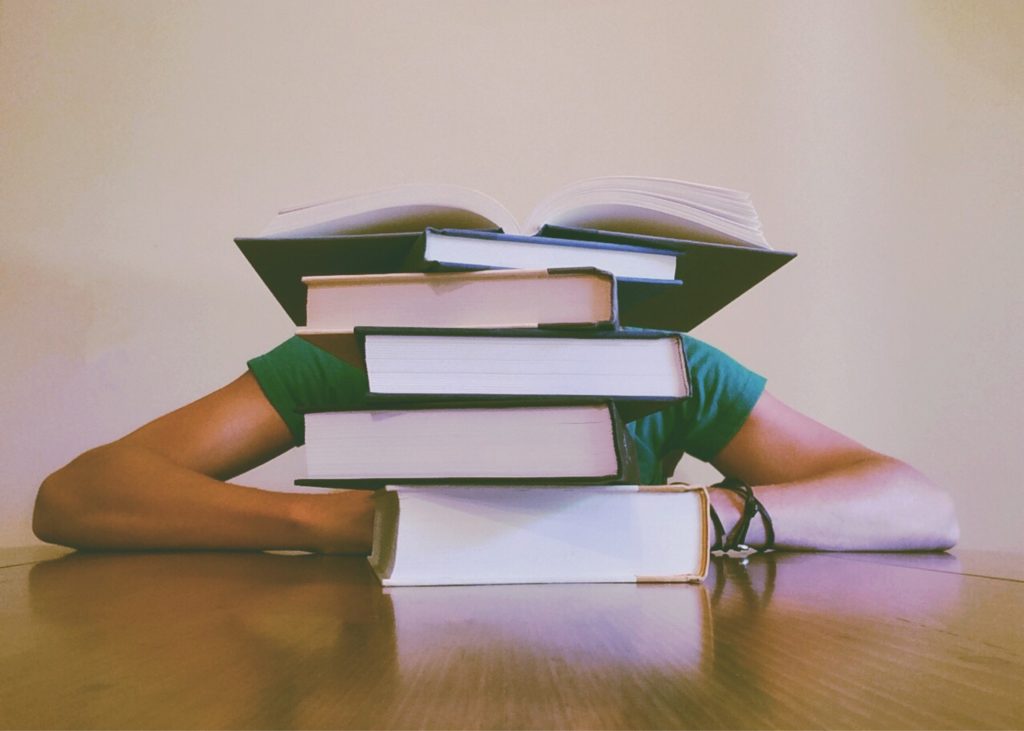 Student with their head down behind a stack of books.