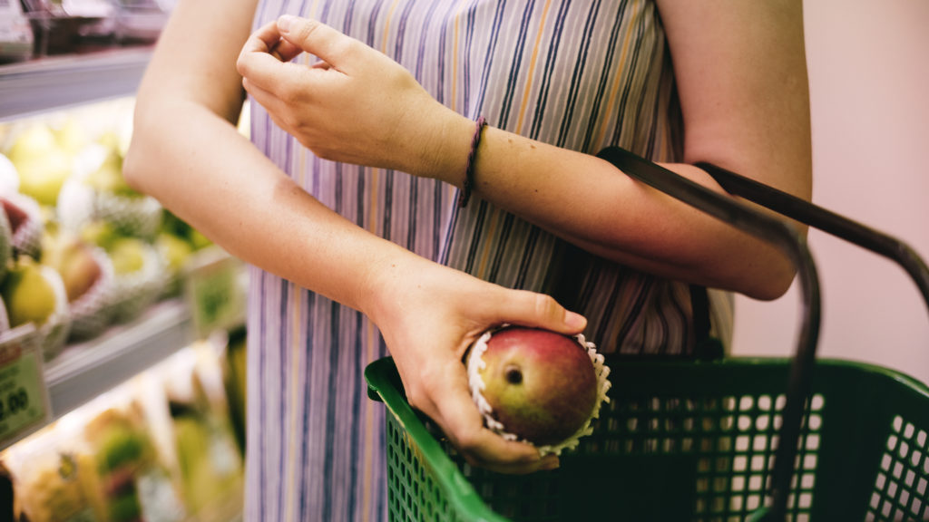 A woman at the grocery store placing an apple in a shopping basket.