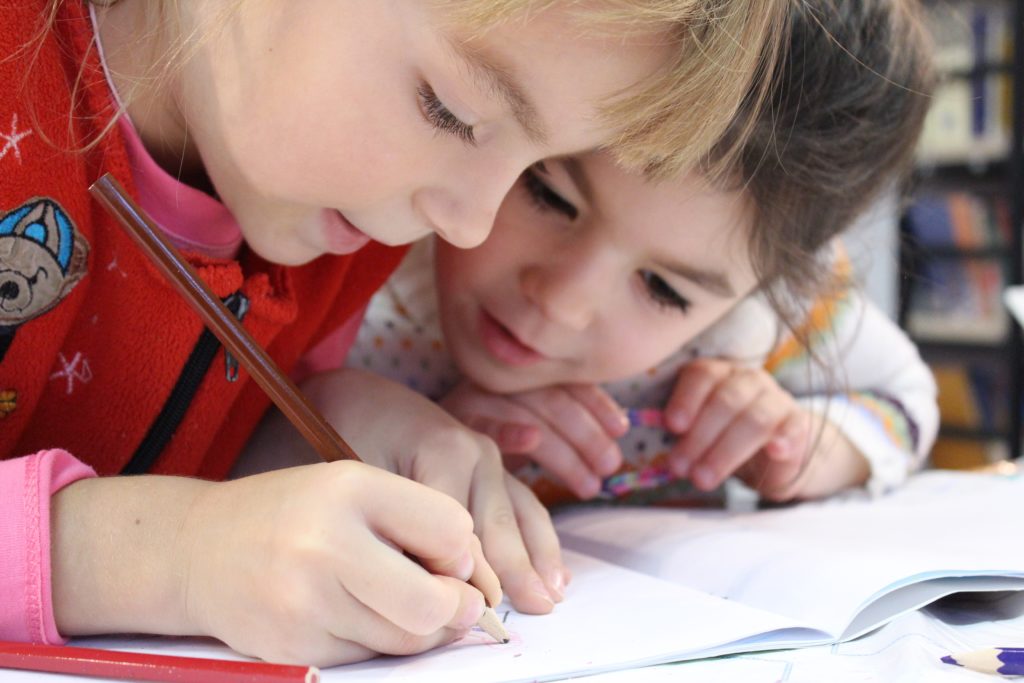 Two young children writing in a book in a library setting.