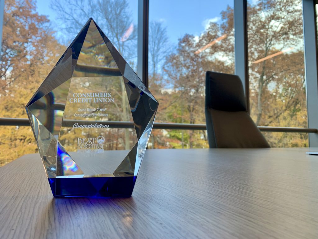A glass Best & Brightest award earned by Consumers Credit Union on a conference table in front of a large window.