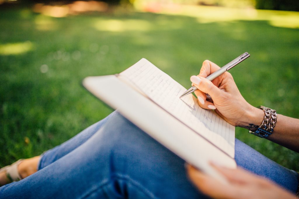 A woman sitting in the grass with a journal resting on her knees while she writes.