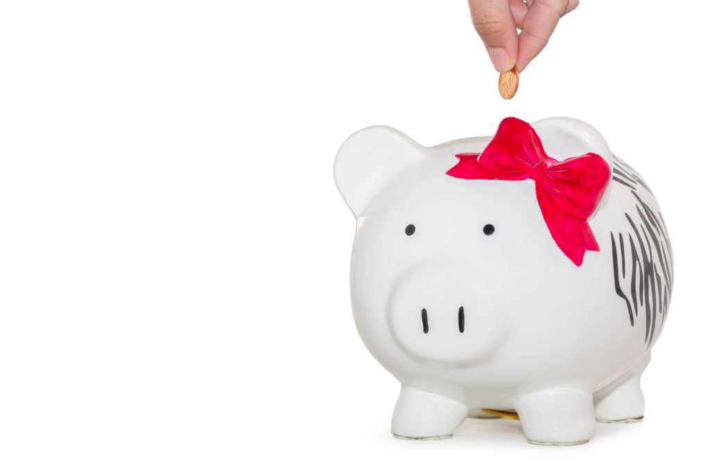 A hand dropping a penny in a black and white piggy bank with a red bow.