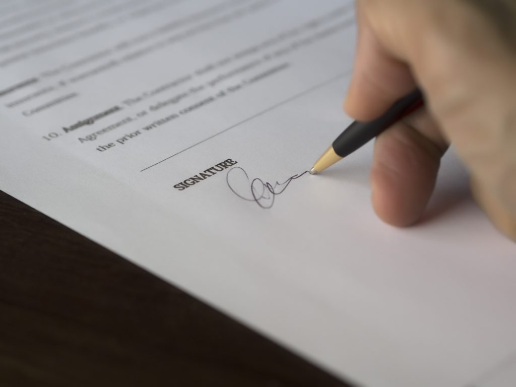 Someone's hand signing a contract with a black and gold pen.