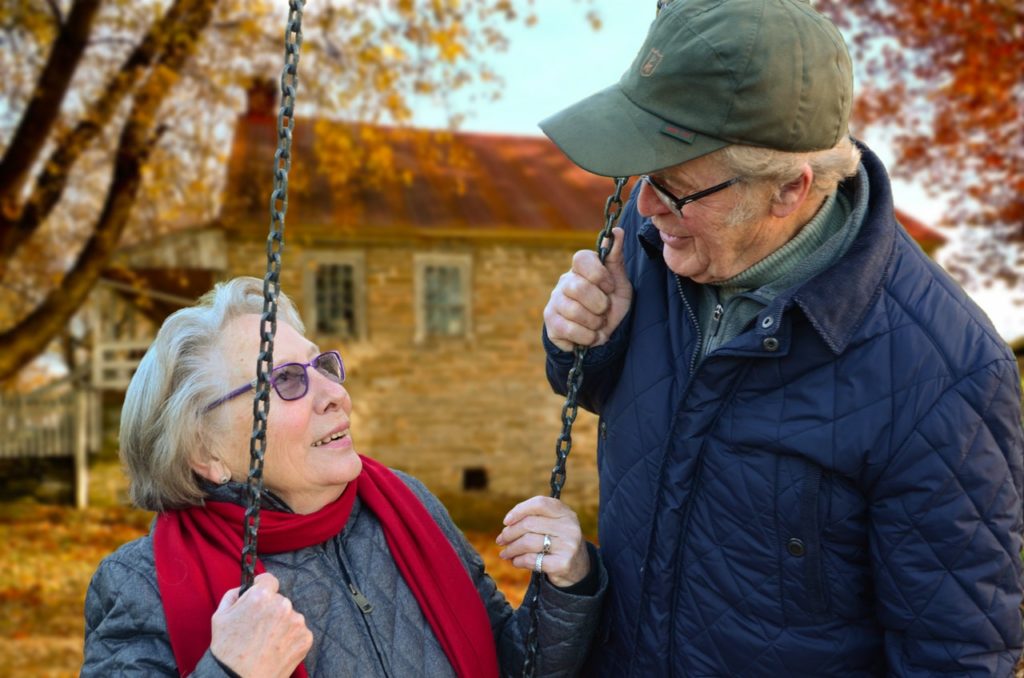 An elderly couple conversing at a swing on a brisk autumn day.