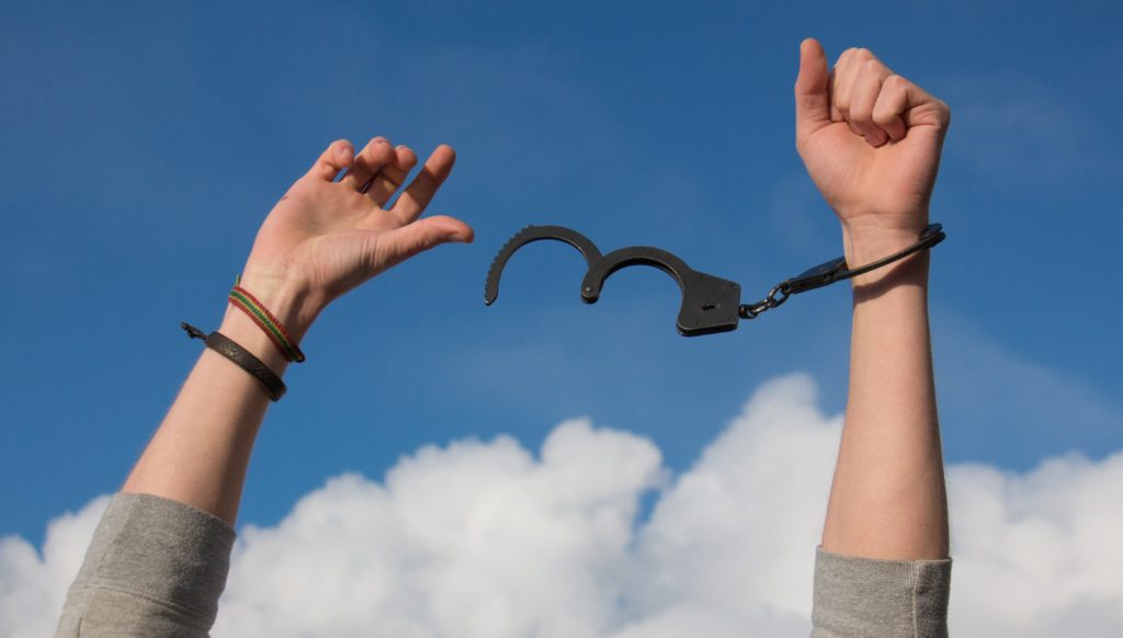 A pair of hands being freed from black handcuffs.