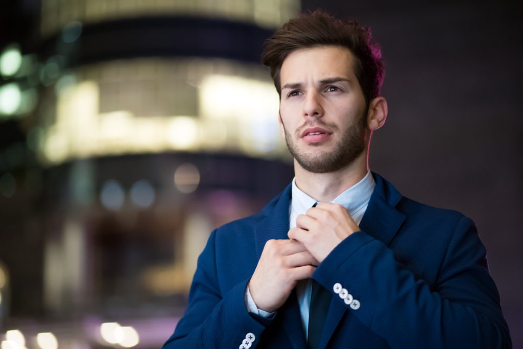 A young man wearing a blue blazer adjusting his tie.