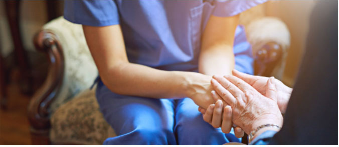 A healthcare provider wearing scrubs holding hands with an elderly person.
