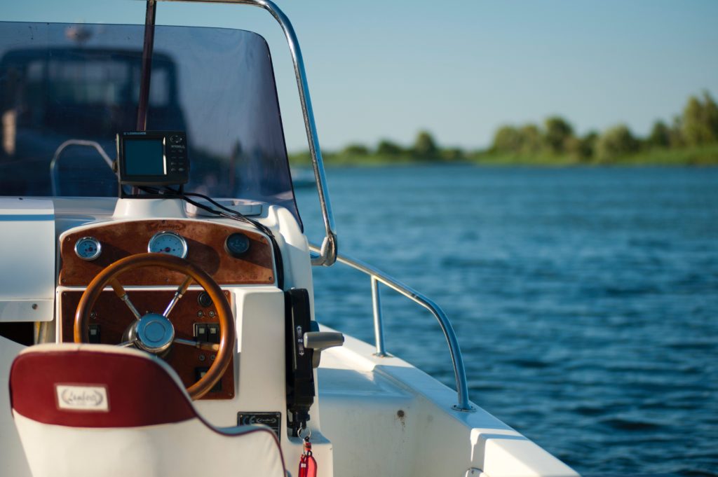 A white boat's captain's chair and steering console with wood paneling on open water.