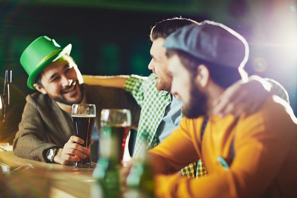 Three men sitting at a bar arm-in-arm celebrating St. Patrick's Day.