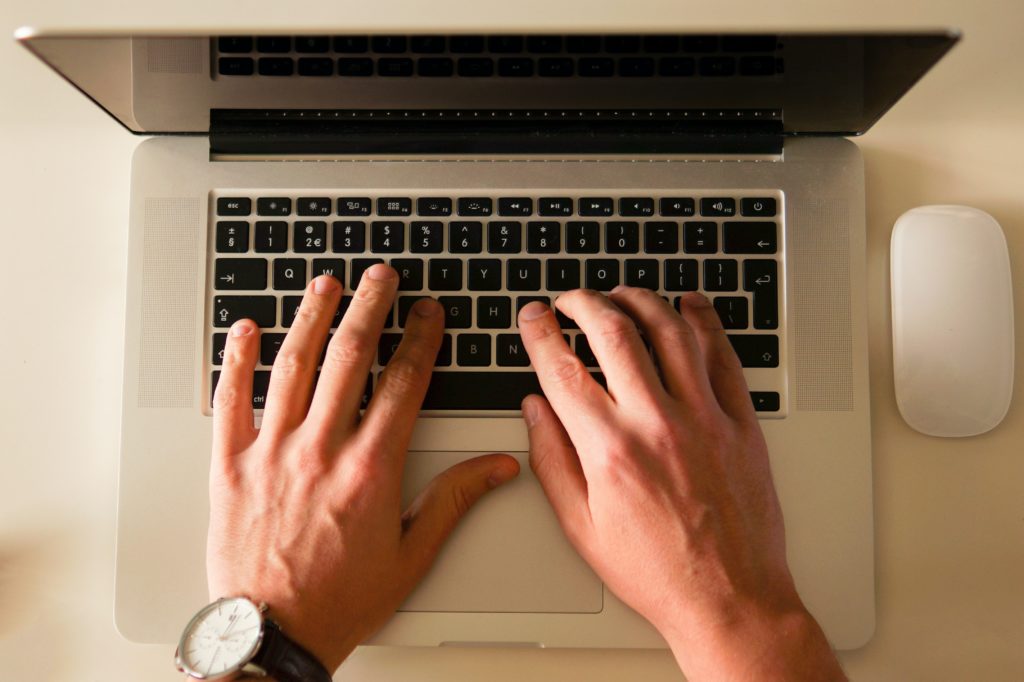 Hands typing on a laptop on a white table.