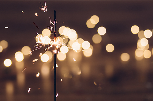 A sparkler alight in the evening with other lights shining in the background.