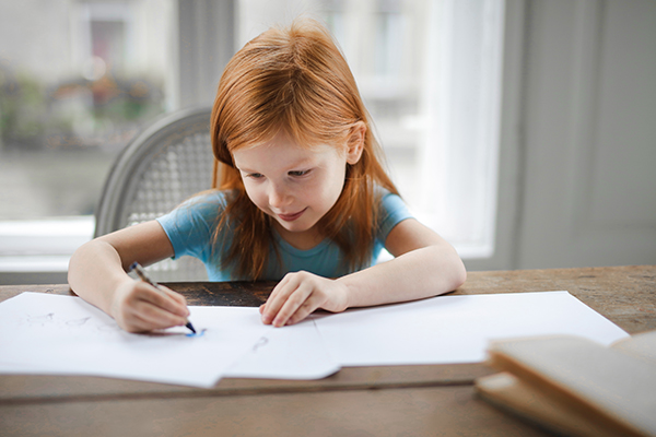 Young girl writing on paper at kitchen counter.