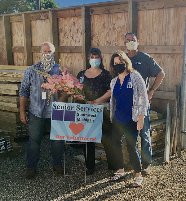 Group of four Senior Services employees holding flowers next to Senior Services yard sign