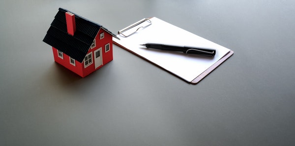 Small red toy house sitting next to a white pad of paper and pen