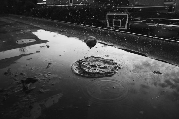 A tennis ball bouncing in a puddle on a rainy day, rippling the water.