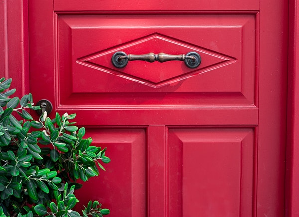 A red door with an ornate handle in the middle of the door.
