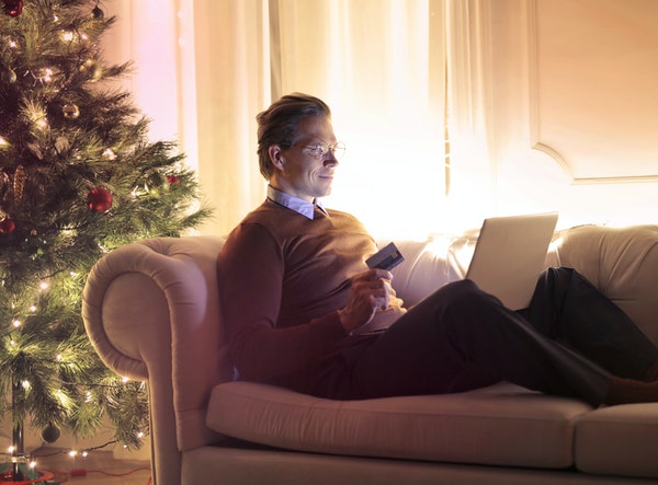 Man online shopping on his couch next to a Christmas tree