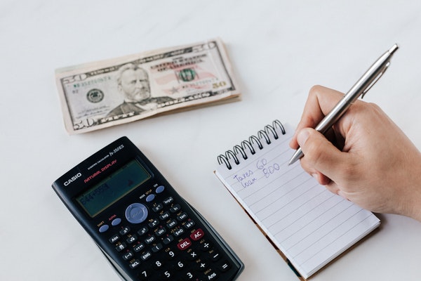 Person writing on a notepad next to a calculator and stack of money