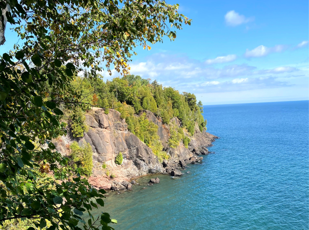 Rocky cliffs with green trees on the edge of a lake on a sunny day in Marquette, Michigan.