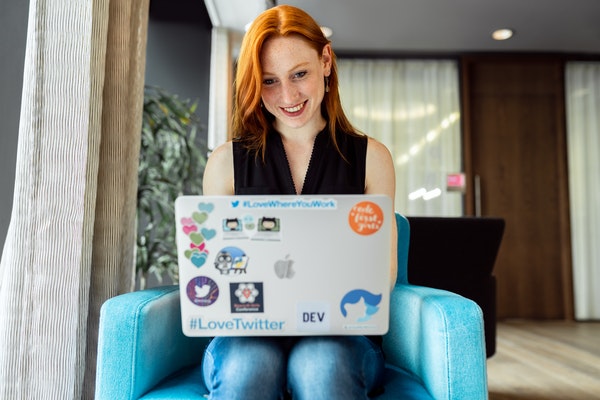Young woman with red hair sitting in blue chair and working on laptop