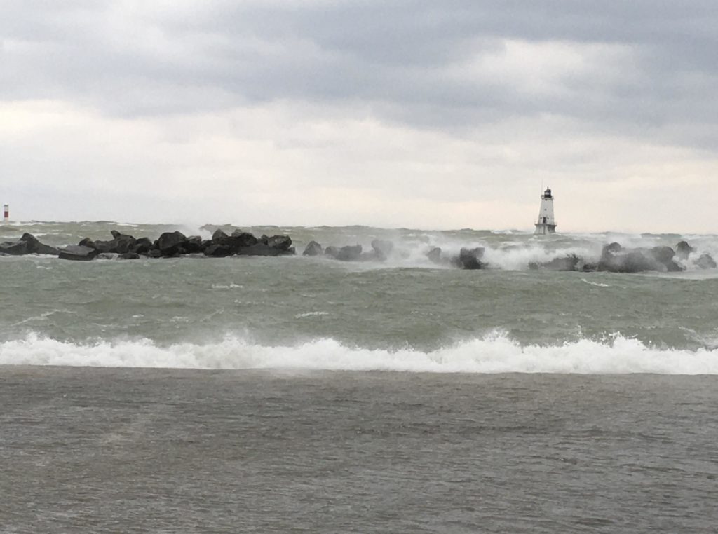 Rough waves crashing on rocks on a cloudy day with a lighthouse and a buoy on the horizon in Ludington, Michigan.