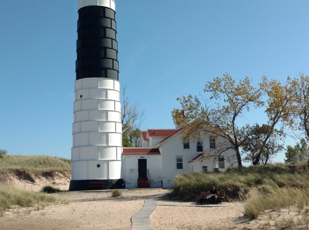 A black and white lighthouse by a white house with a red roof in Ludington State Park in Michigan.