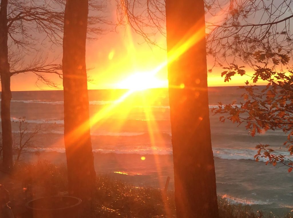 Sunset peeking through trees on a lake in Manistee, Michigan in the autumn.