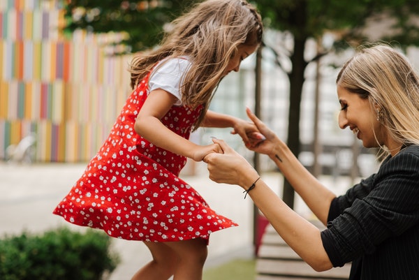 Mother holds hands of daughter in red dress jump down