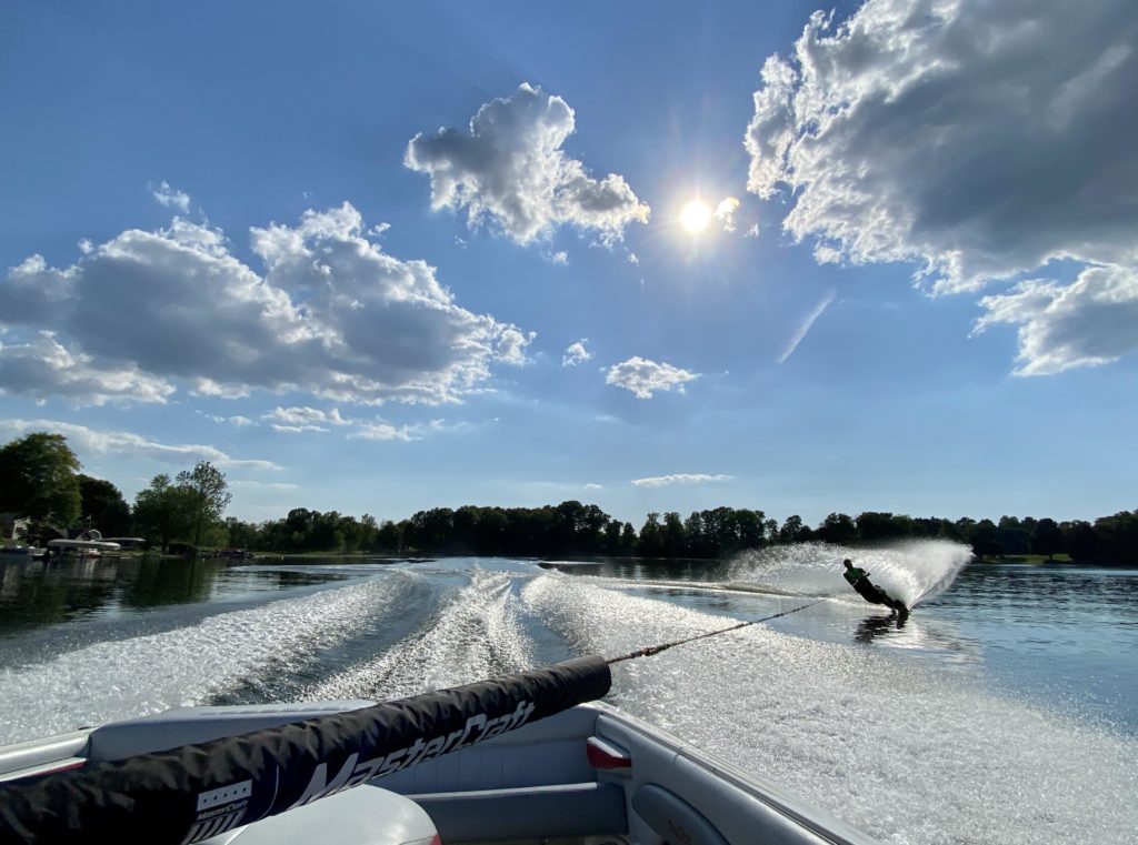 A motorboat pulling a wakeboarder on a Reynolds Lake in Lawrence, Michigan on a sunny summer day.