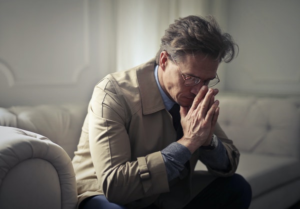Older business gentleman sitting on couch with head in hands