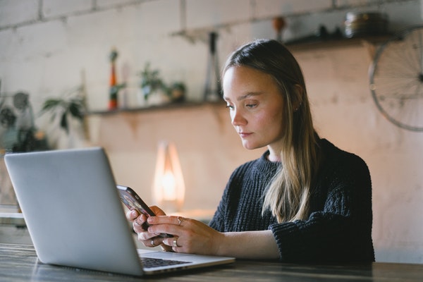Serious looking woman looking at her phone while on her laptop