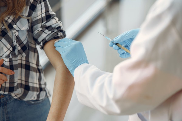 Medical professional in white coat wearing blue gloves giving an vaccination