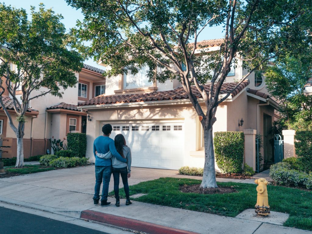 Couple standing on a sidewalk looking up at a house.