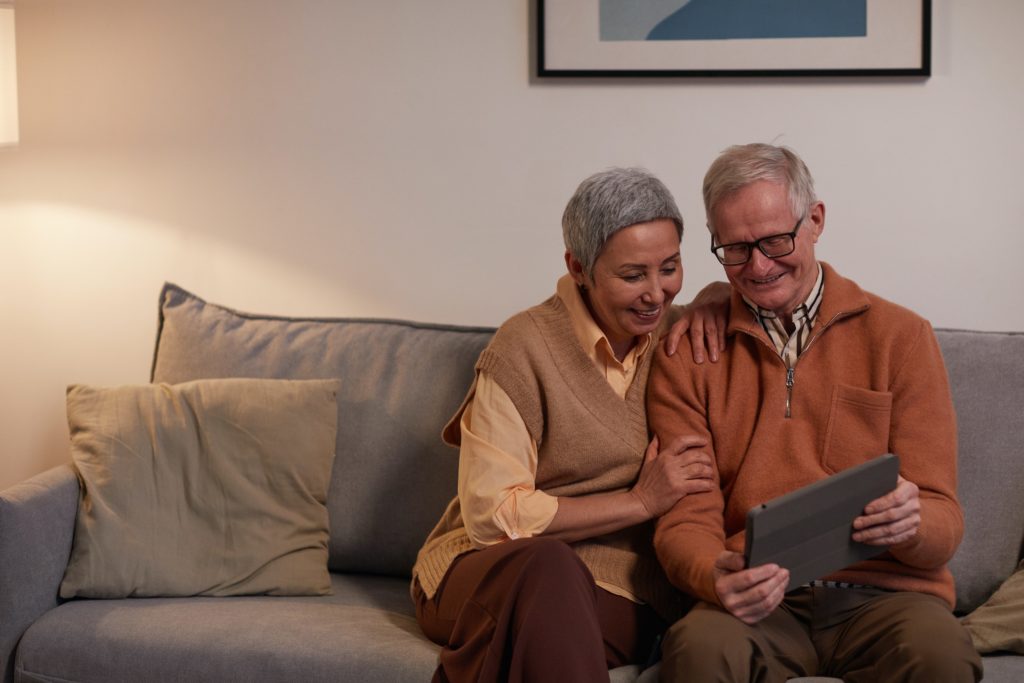 Older couple sitting on a sofa and looking at a computer.