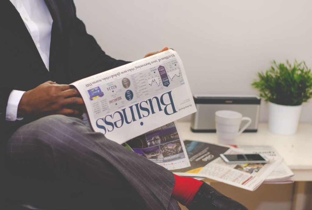 Person sitting in a chair reading the business section of a newspaper.